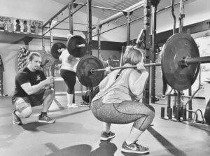 A woman completes a squat while an Elite Edge trainer supervises.